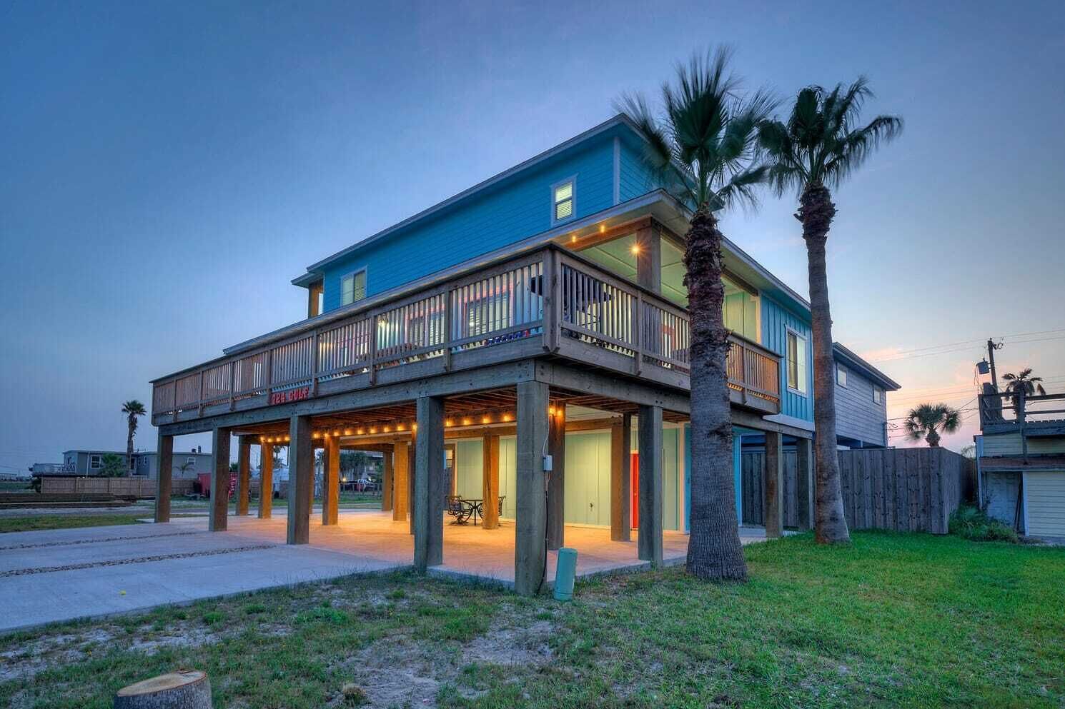 A two-story beachfront house with a balcony and outdoor lighting.