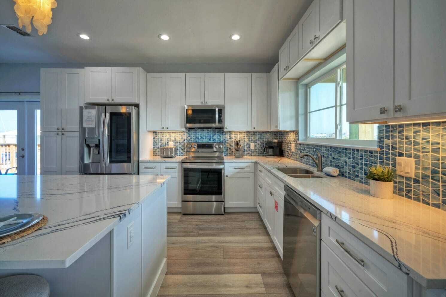 A modern kitchen with white cabinetry, stainless steel appliances, a large island, and a blue mosaic backsplash.