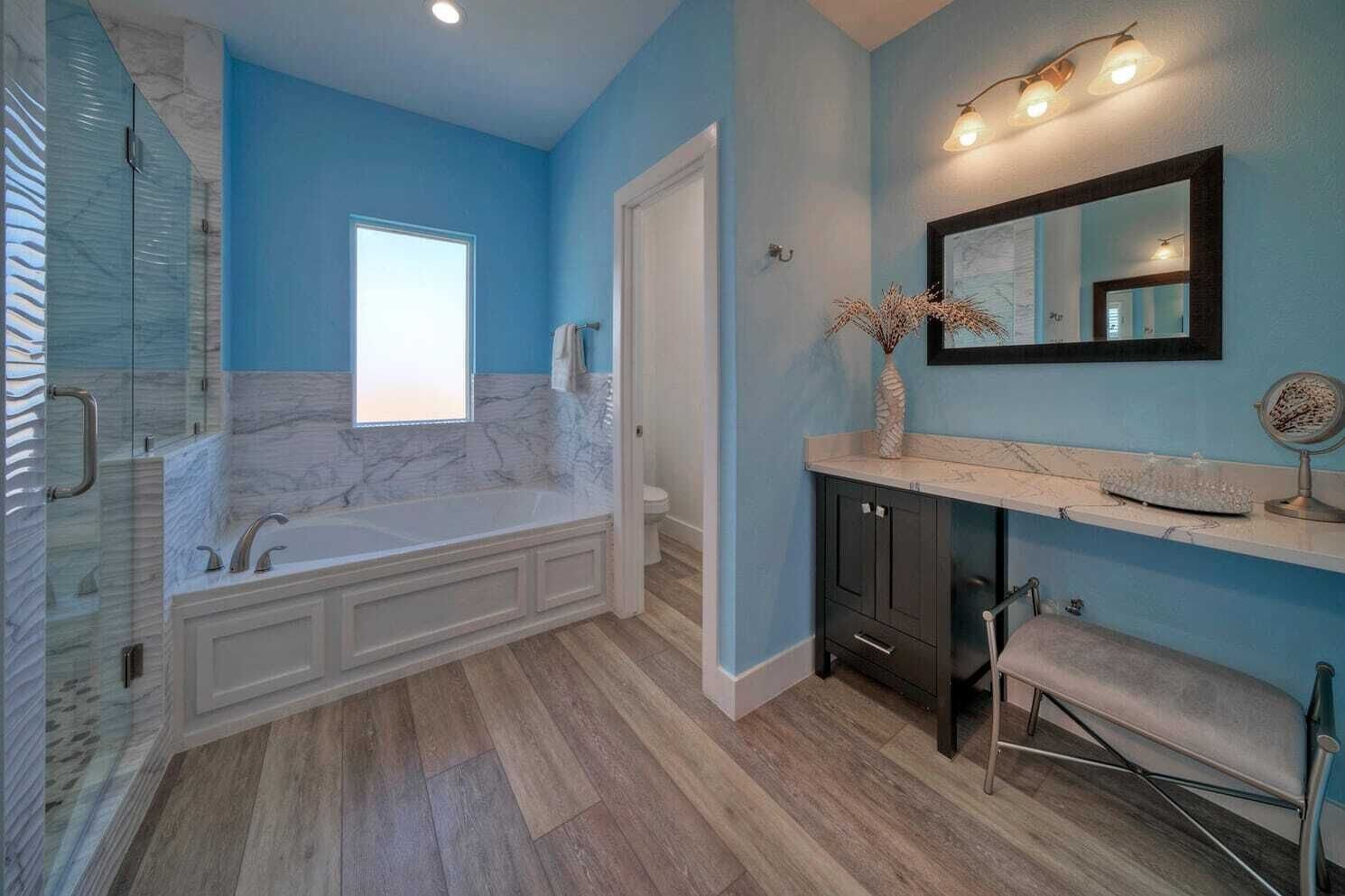 Ein Badezimmer mit einer Marmorbadewanne, einem Schminktisch mit Spiegel und einer Duschkabine mit Glastür.