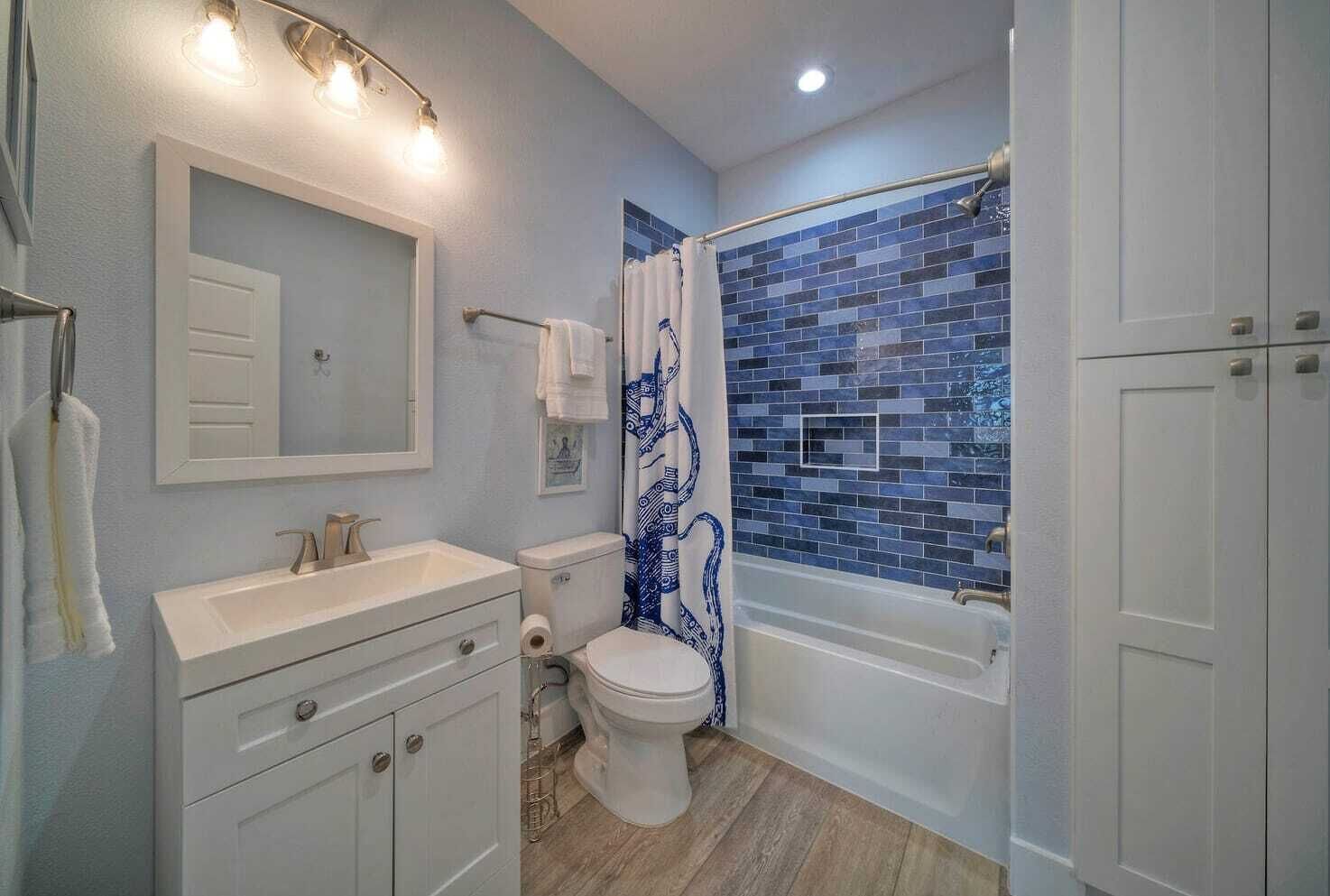 A bathroom with a white vanity, a toilet, and a bathtub with a blue mosaic tile wall.