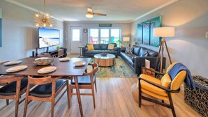 A living room with a dining area, a sofa set, a coffee table, a television, and a ceiling fan. - Beach Boardwalk, Gulf View, Pool, Tennis+pickleball Beach Please! by Avantstay (Port Aransas)