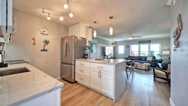 A modern kitchen with a large island, a refrigerator, and a dining area with a sofa and coffee table. - Beach Boardwalk, Gulf View, Pool, Tennis+pickleball Beach Please! by Avantstay (Port Aransas)