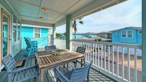 Una terraza de madera con una mesa y sillas, una mesita con un objeto decorativo, y una vista de casas azules al fondo.