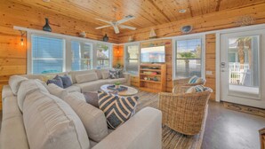 A cozy living room with a wooden ceiling, a large sofa, a wicker chair, and a bookshelf. - Gated Community w/ Pool 5mins to Beach Latitude Adjustment by Avantstay (Port Aransas)