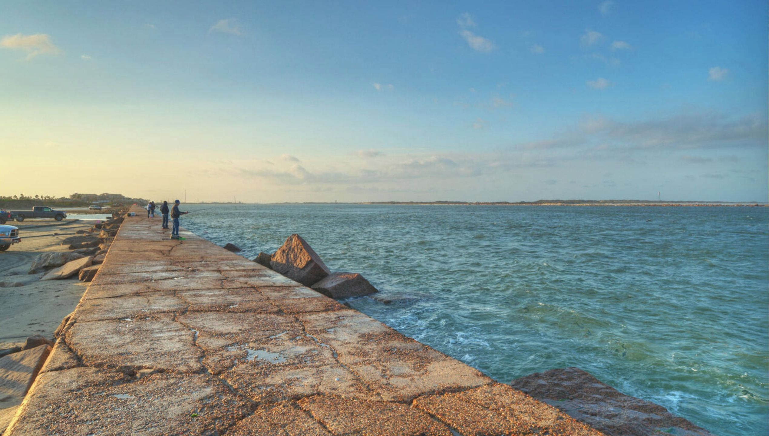 Un muelle costero con paseo de hormigón, grandes rocas y mar tranquilo.