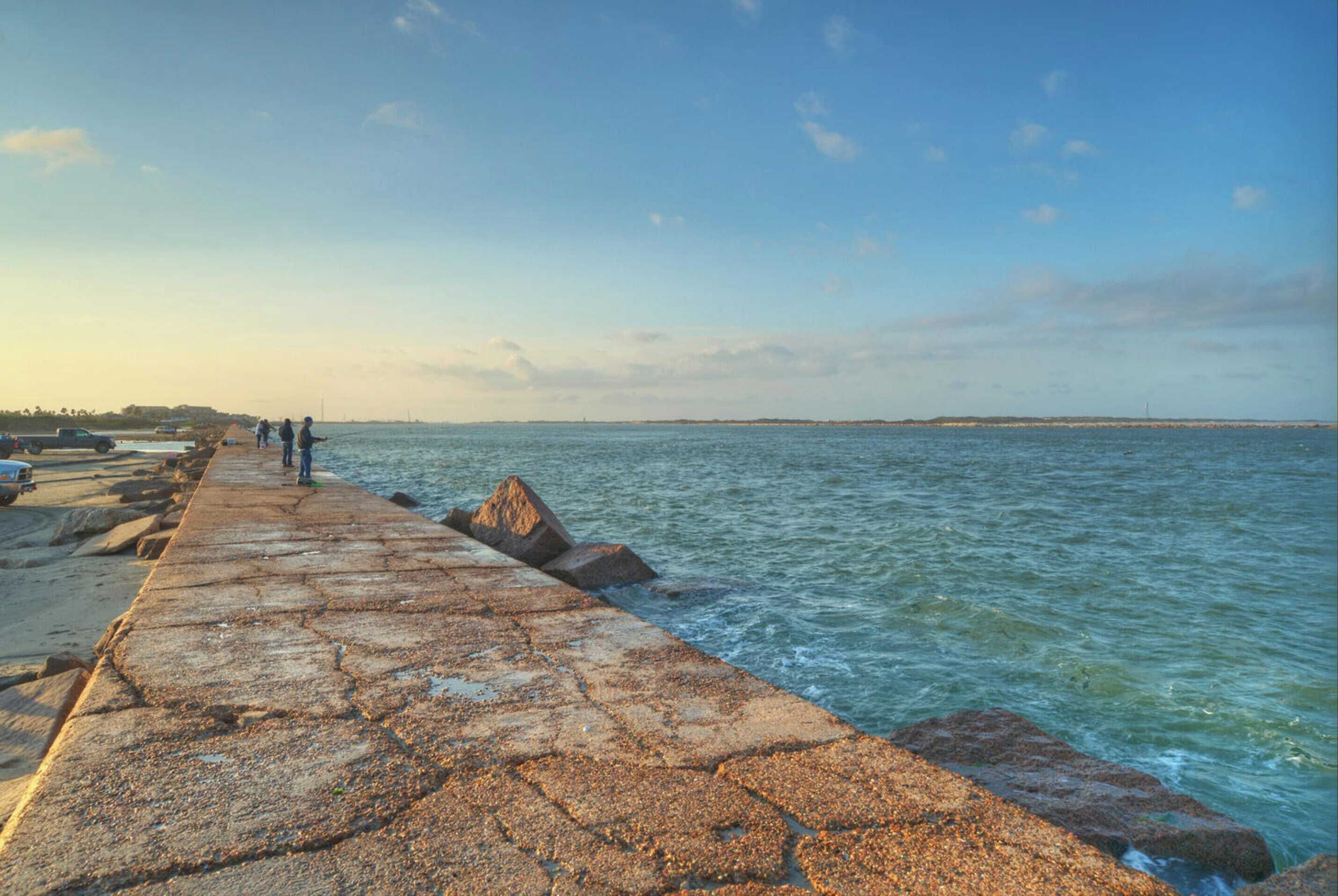 A stone pier extending into calm waters with a clear sky.