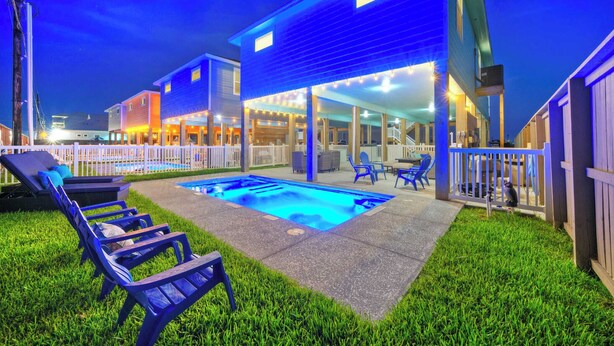 Un patio trasero con piscina, sillas de descanso y un área de patio techada.