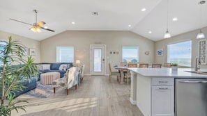 A spacious living area with a sofa, chairs, a dining table, and a kitchen area with a sink and cabinets.