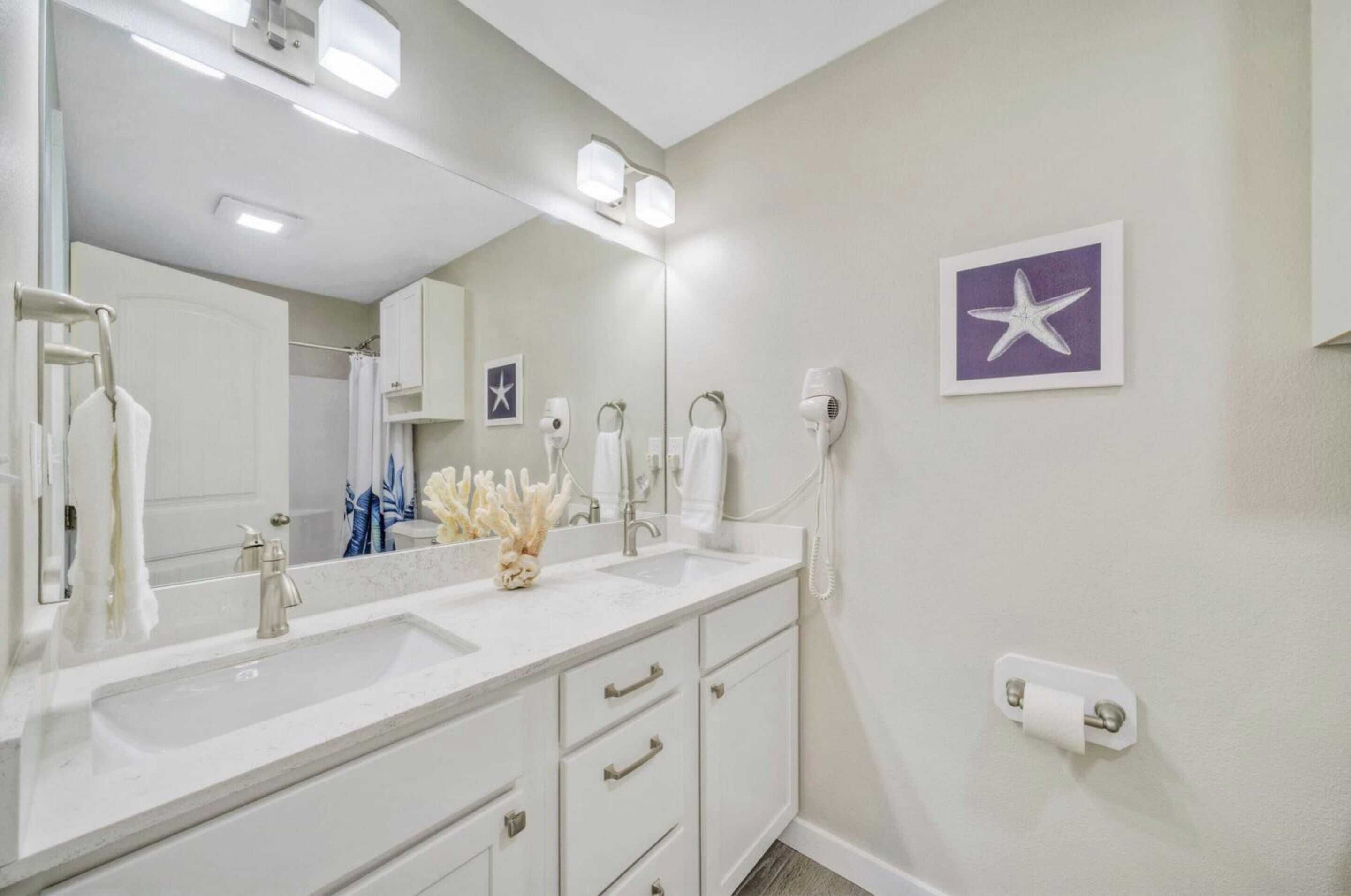 A bathroom with a large mirror, two sinks, a hairdryer, and a towel rack.