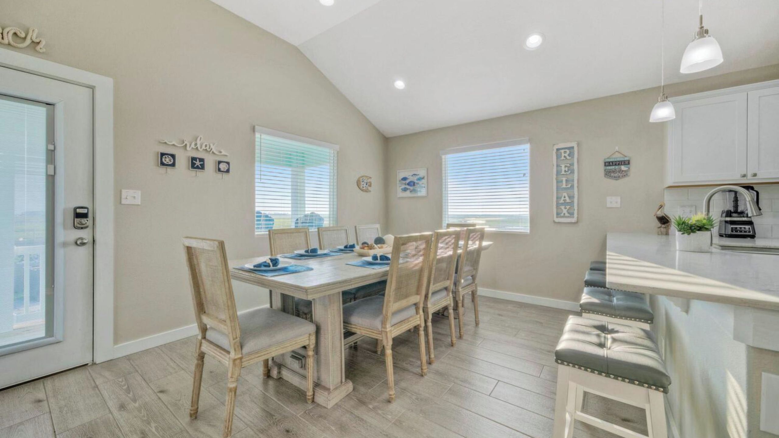 A dining area with a wooden table and chairs, a kitchen with white cabinets, and a view of the outside.