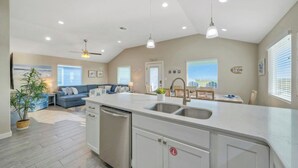 Una cocina amplia con una isla central, un comedor con vistas y una sala de estar con sofá y cojines decorativos.