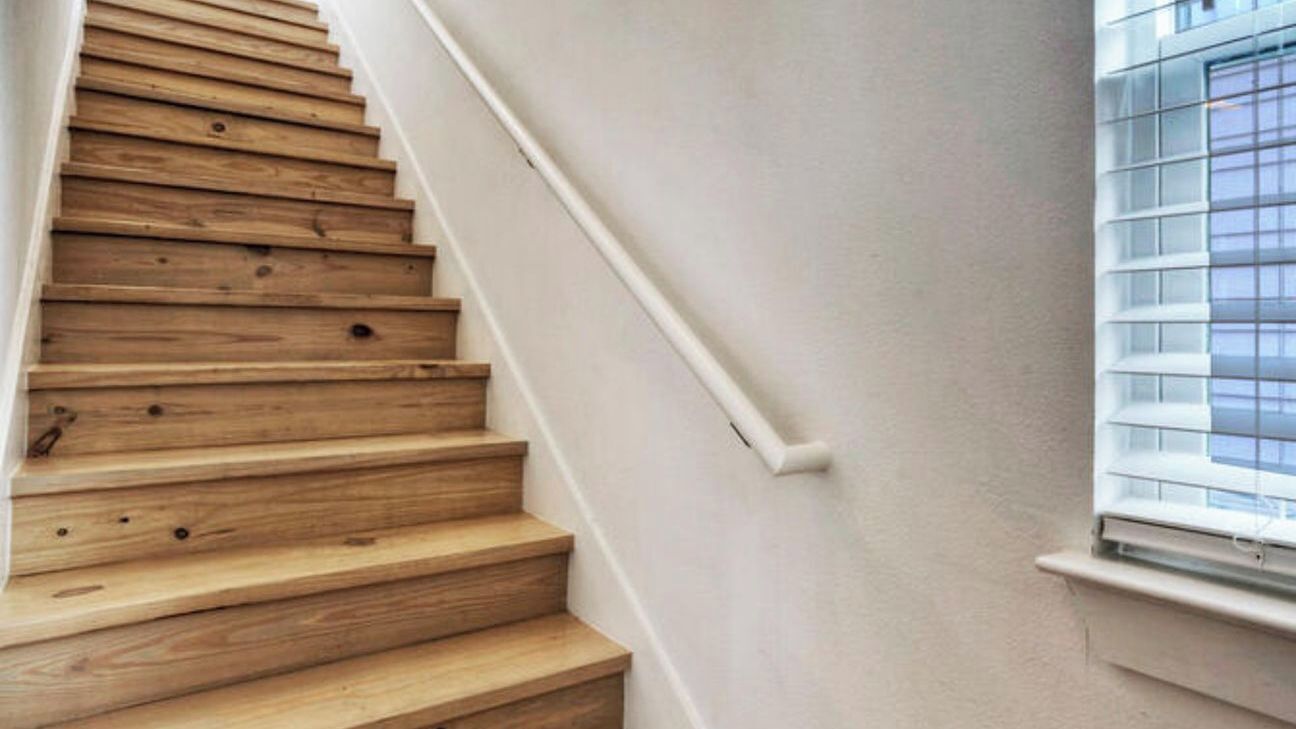 A wooden staircase with white walls and a window with blinds.