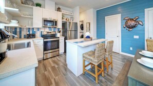 A modern kitchen with white cabinetry, stainless steel appliances, and a blue accent wall. - Pool 1 Block to Alister + Old Town + Eateries Bluegrass Breeze by Avantstay (Port Aransas)