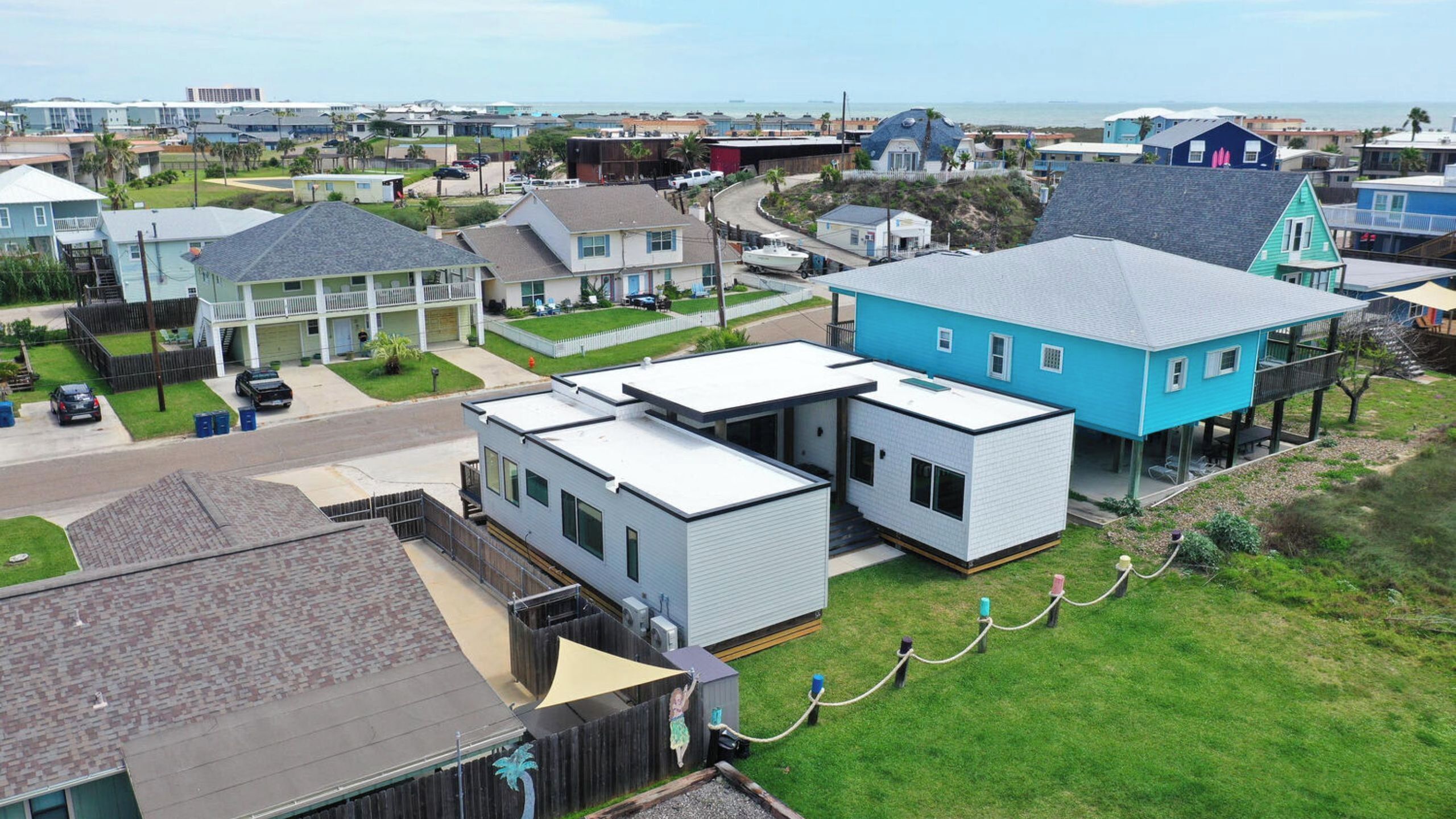 Un quartier résidentiel avec des maisons modernes, une route bien visible et une vue lointaine sur l’océan.