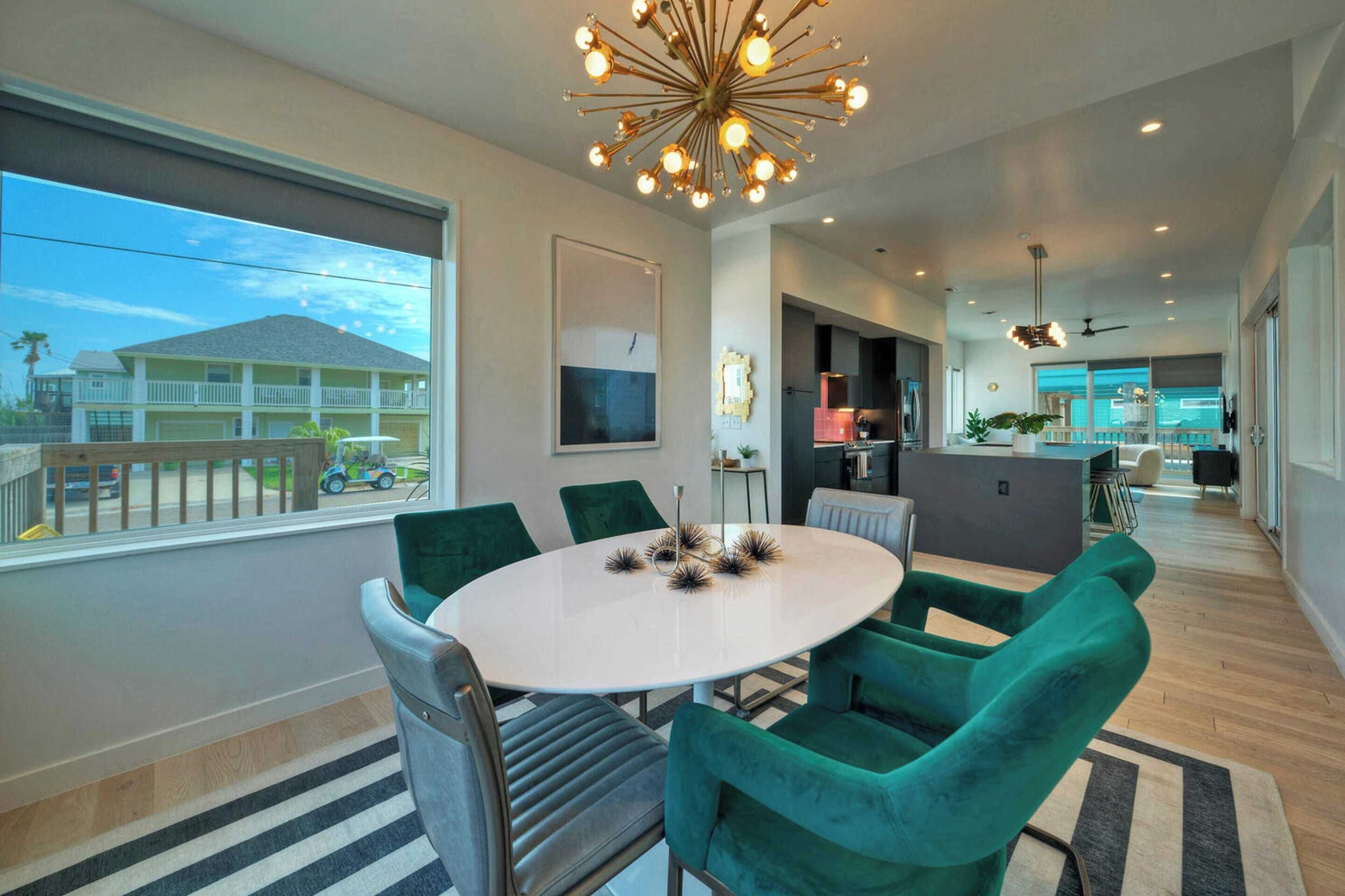 A modern dining area with a round table, green chairs, and a decorative ceiling light.