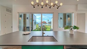 A modern kitchen with a stainless steel sink, a chandelier, and a view of the backyard. - Modern Design, 3 Mins to the Beach Boat Parking The Beach Box by Avantstay (Port Aransas)