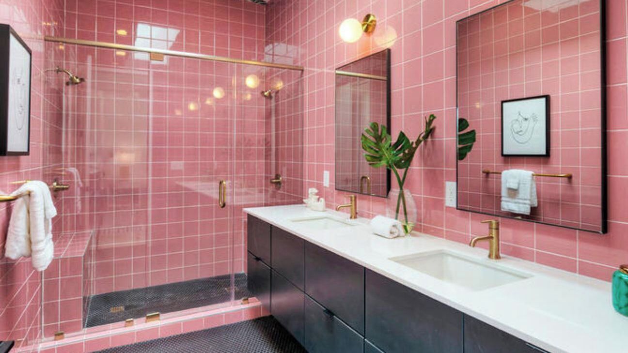 Un baño moderno con azulejos rosas, cabina de ducha de vidrio y tocador con dos lavamanos y un espejo.