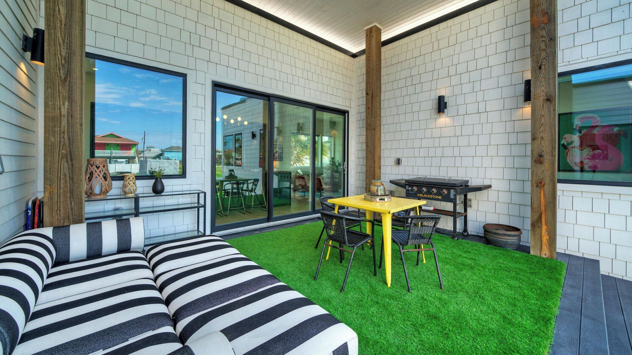 A modern patio with a striped sofa, a yellow table, and a grill.