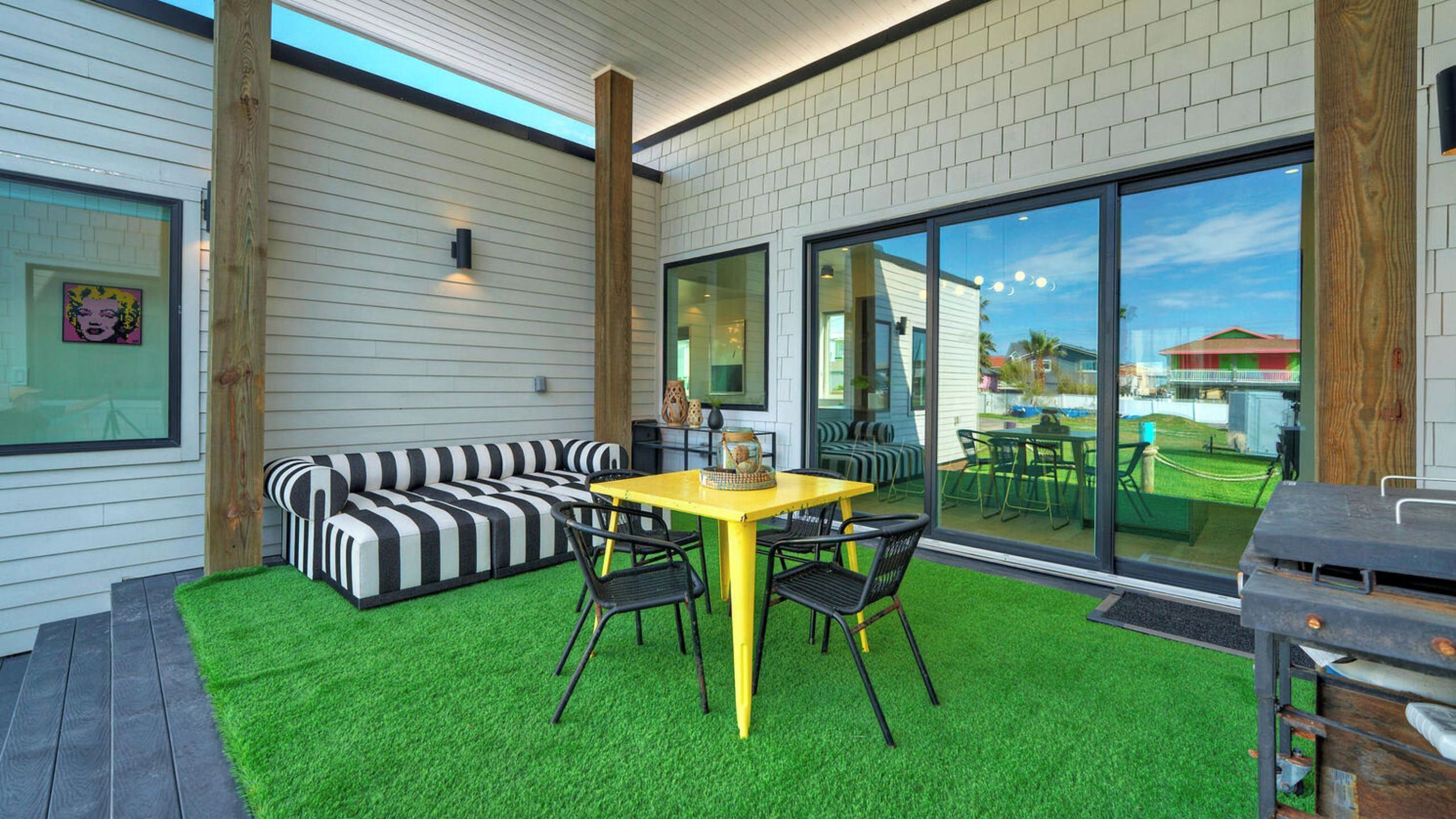 A modern outdoor patio with a yellow table, black and white striped sofa, and a view of the neighborhood.