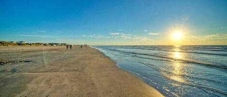 A beach with a clear sky and the sun setting over the horizon.