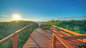 Een houten looppad dat naar een strand leidt, onder een heldere lucht.
