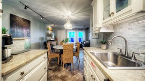 Een moderne keuken met een groot eiland, een rvs-gootsteen en een eethoek met rieten stoelen.