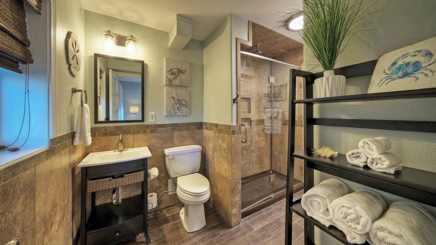 A bathroom with a sink, toilet, shower, and shelves with towels.