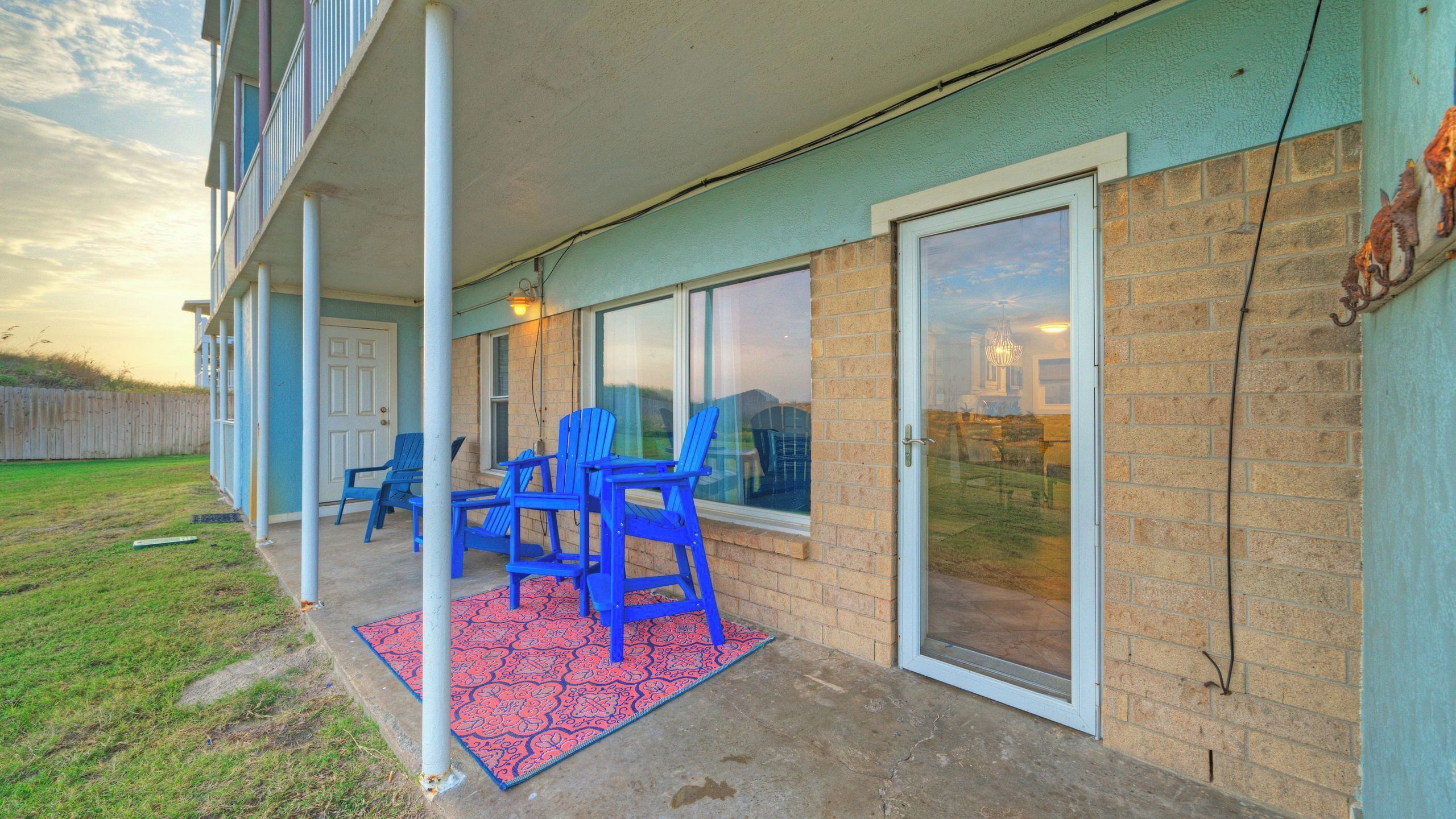 A covered patio with blue chairs and a patterned rug.
