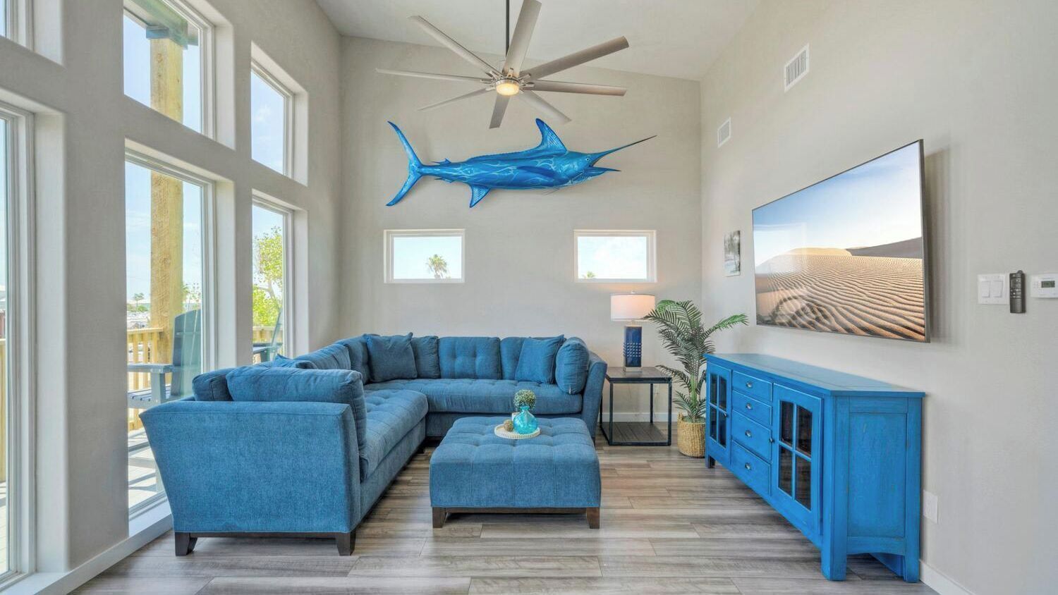 A living room with a sectional sofa, a ceiling fan, a large shark decoration, a TV, and a cabinet.