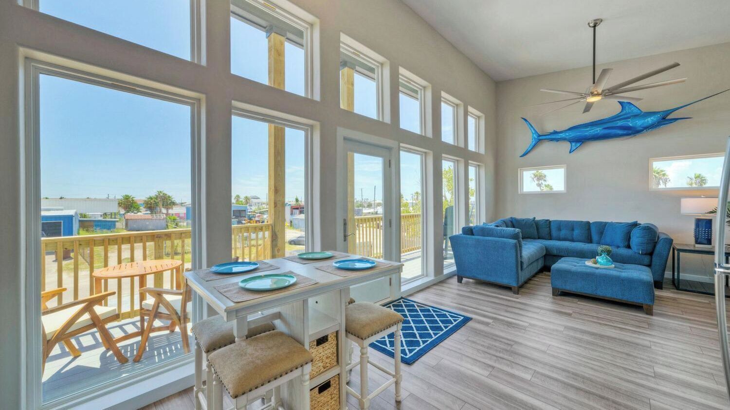 A spacious living area with large windows, a ceiling fan, and a blue shark decoration.