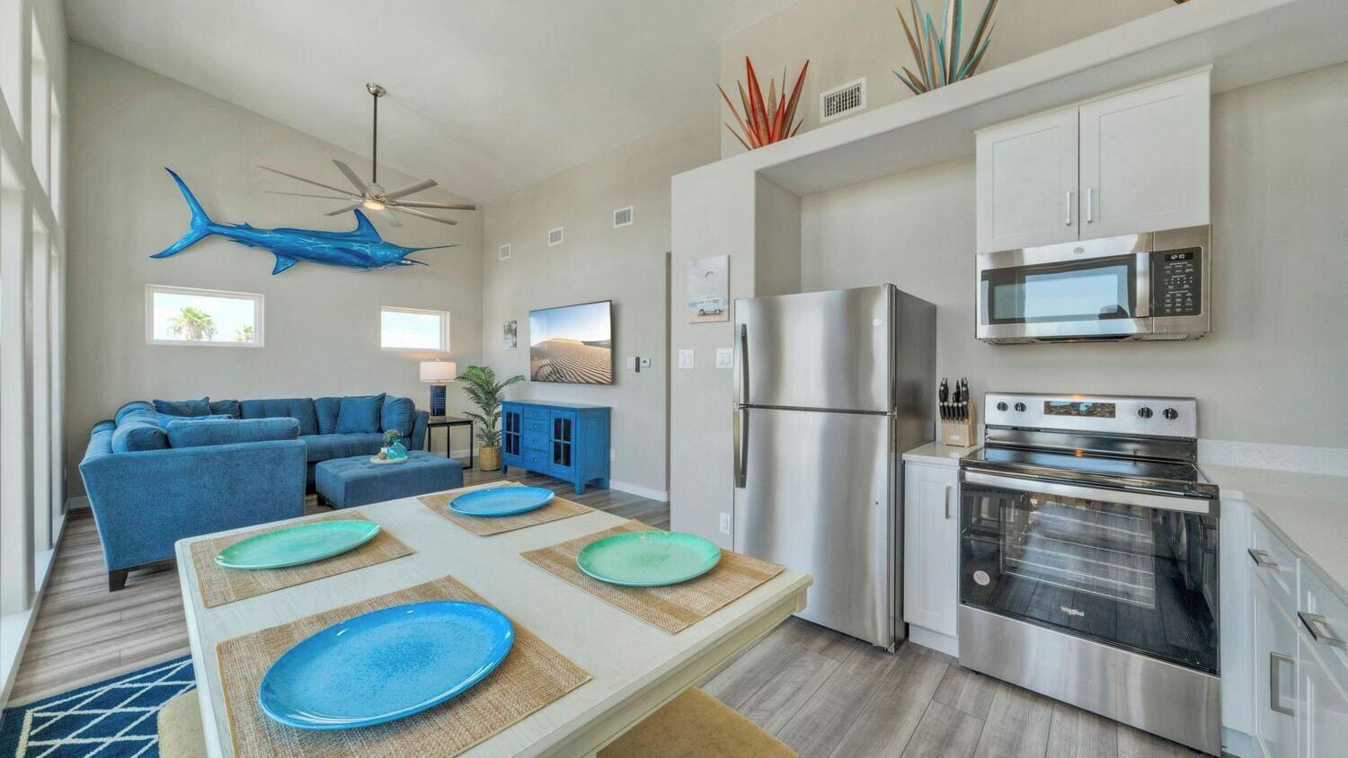 Eine moderne Küche mit Edelstahlgeräten, ein Essbereich mit einem blauen Sofa und einem Deckenventilator.