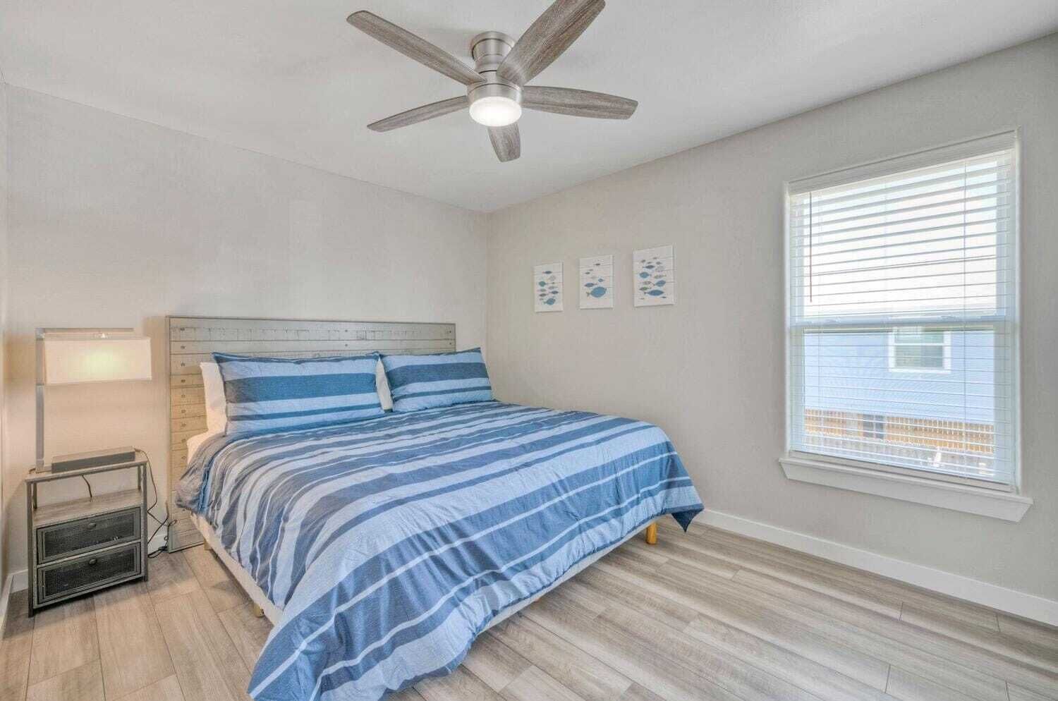A bedroom with a bed, a ceiling fan, a nightstand, and a window with blinds.