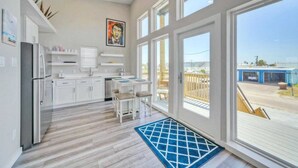A modern kitchen with white cabinets, a dining area with a table and chairs, and large windows offering a view of the outside. - Dean Marlin by Avantstay Stunning Old Town Home! (Port Aransas)
