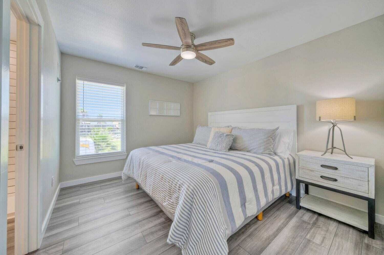 A bedroom with a bed, a nightstand, a lamp, a ceiling fan, and a window.