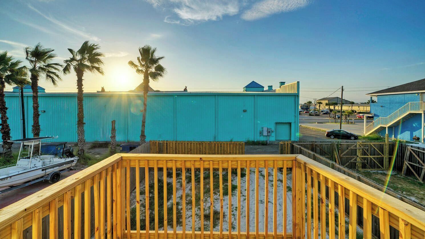A wooden deck with a boat, a turquoise building, and palm trees.