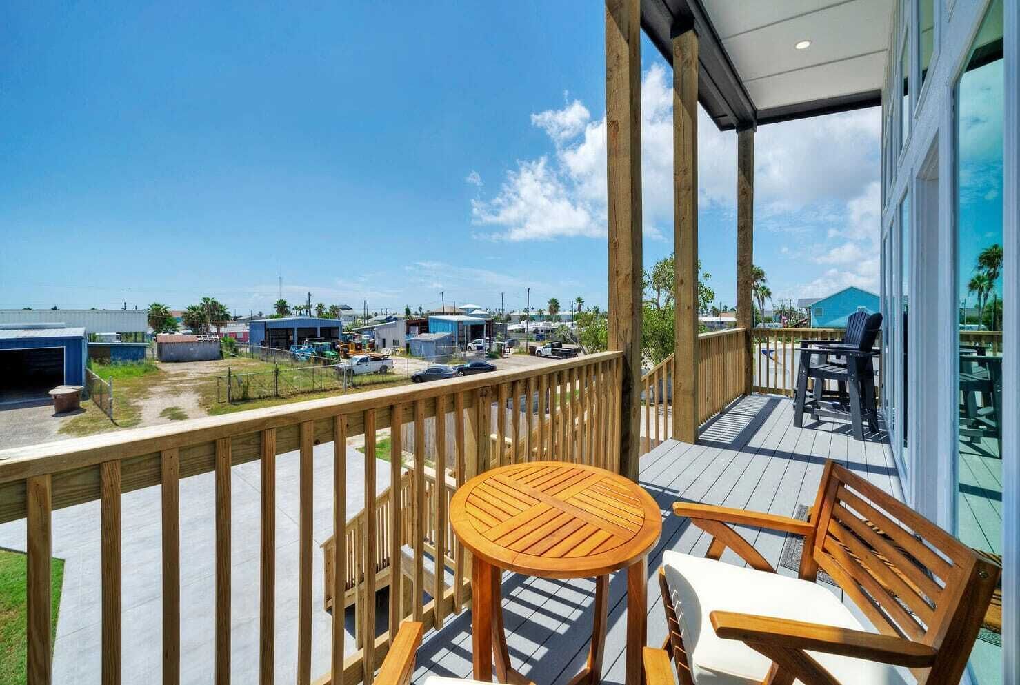 A wooden deck with a round table and chairs, overlooking a parking area and buildings.