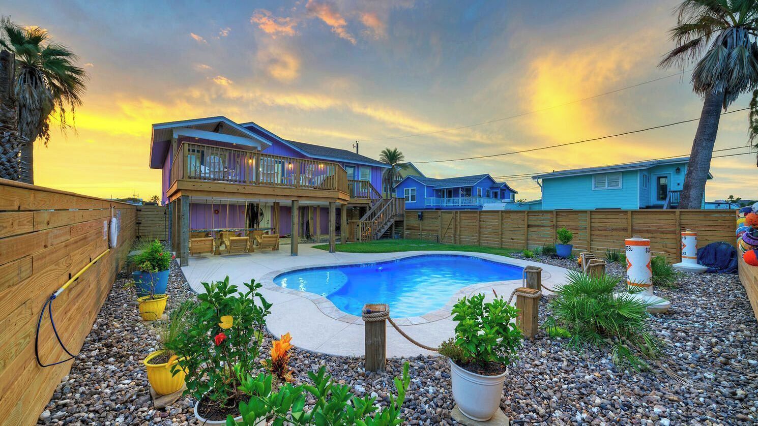 A backyard with a swimming pool, wooden deck, and potted plants.