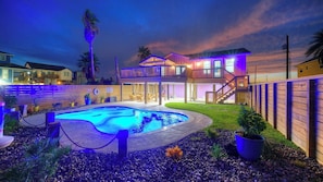 A two-story house with a swimming pool, a covered patio, and a wooden fence.