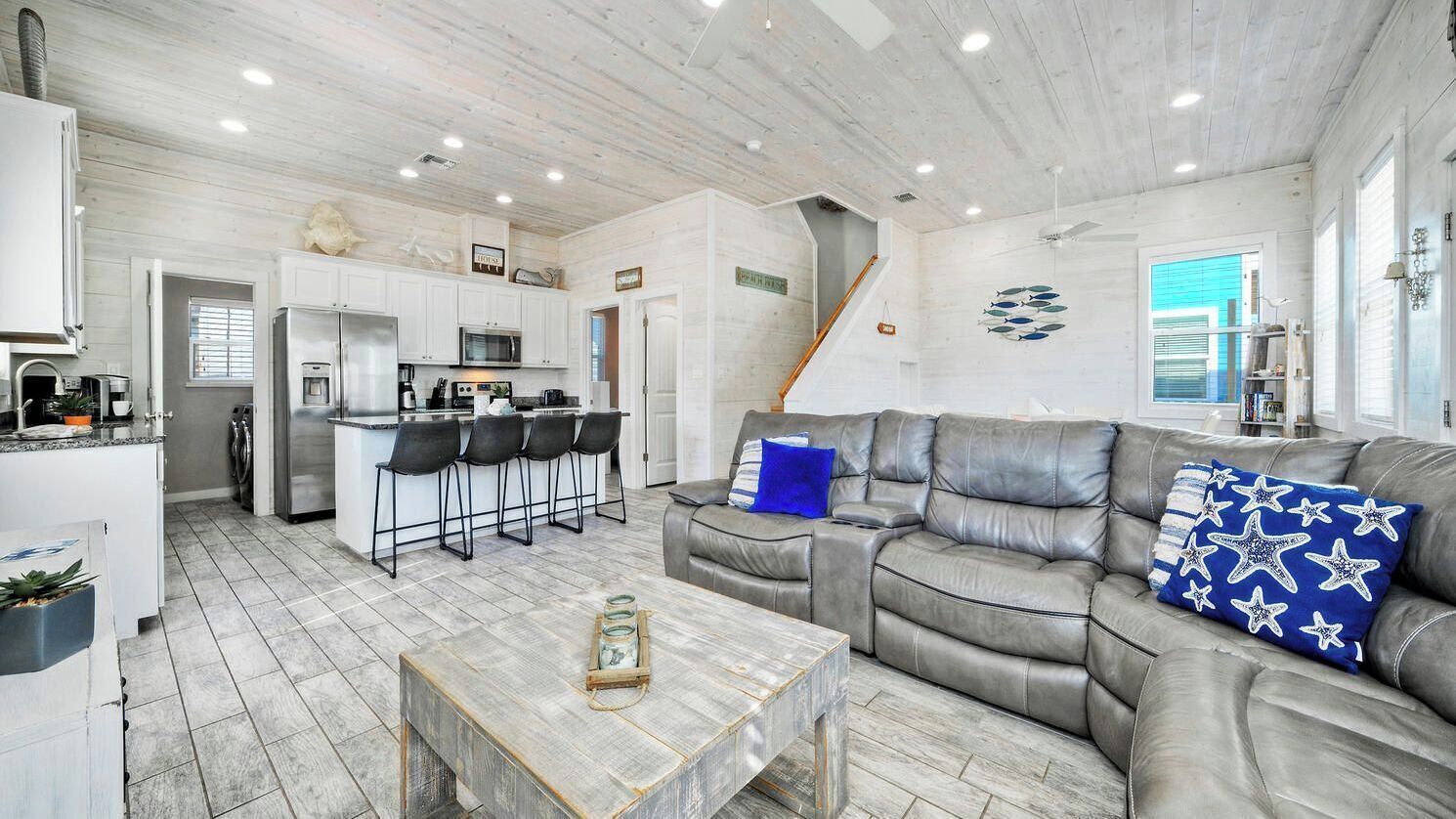 A modern kitchen with a bar area, a grey leather sofa, and a coffee table.