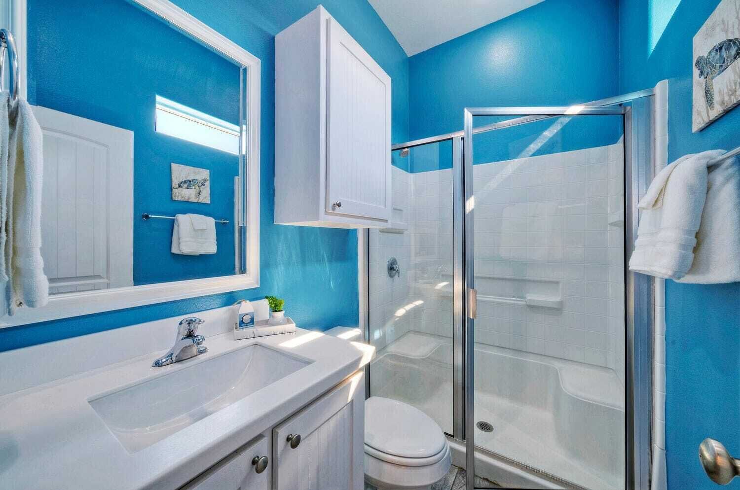 A bathroom with a blue wall, white fixtures, a glass shower enclosure, and a toilet.