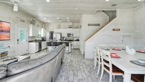 A modern kitchen with white cabinets, a dining area with a white table and chairs, a leather sofa, and a staircase leading to another level. - 2 Blocks to the Beach, Pool, Patio w/ Bar Awave From it All by Avantstay (Port Aransas)