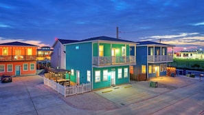 A two-story building with a balcony, a car parked in front, and a white fence. - 2 Blocks to the Beach, Pool, Patio w/ Bar Awave From it All by Avantstay (Port Aransas)