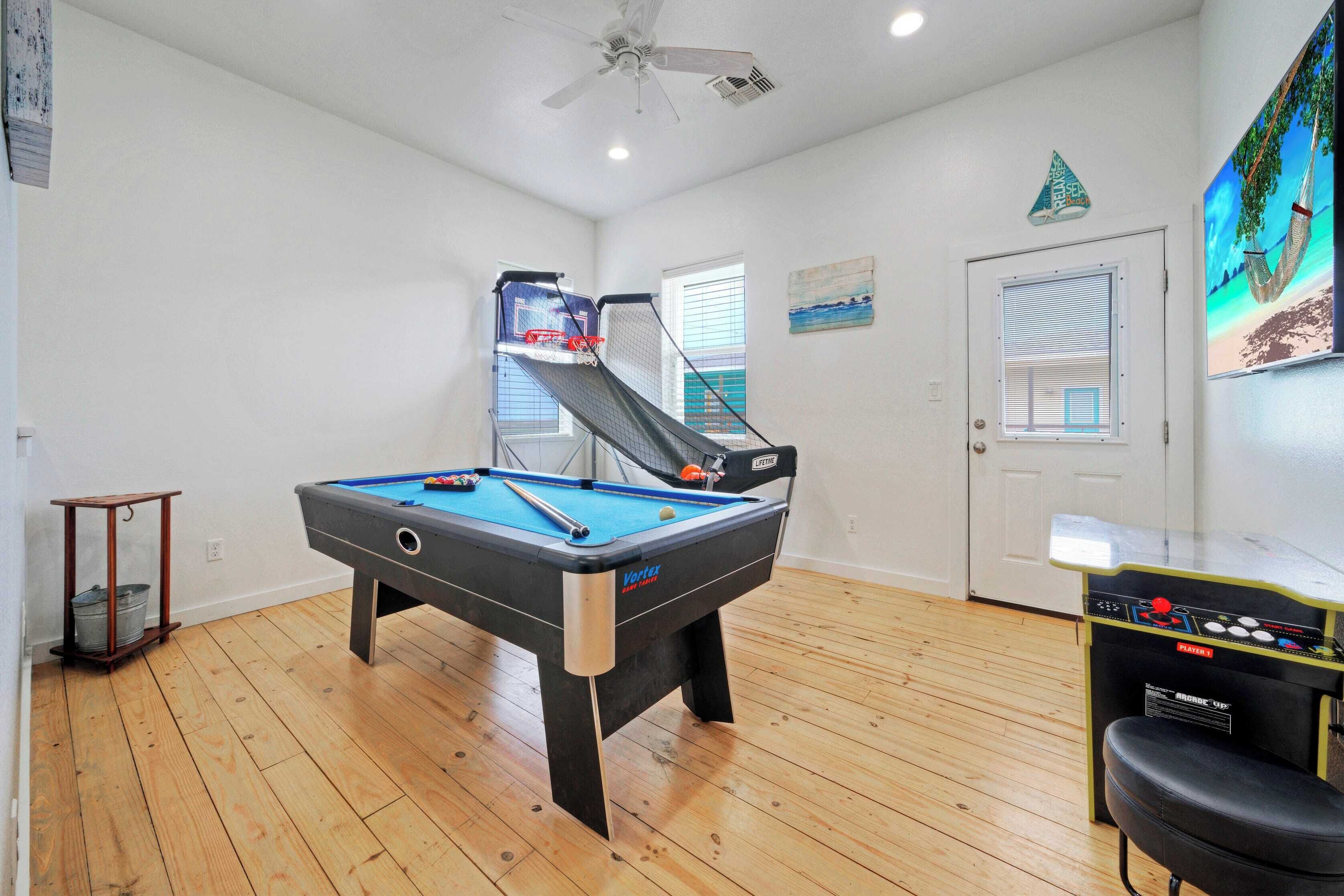 A pool table in a room with wooden flooring, a ceiling fan, and a door with a window.