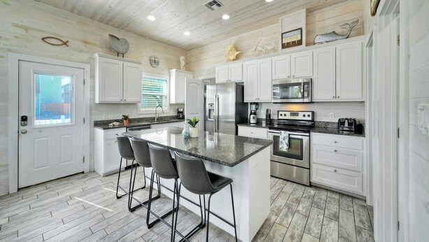 A kitchen with white cabinets, a central island with bar stools, stainless steel appliances, and a wooden ceiling. - 2 Blocks to the Beach, Pool, Patio w/ Bar Awave From it All by Avantstay (Port Aransas)