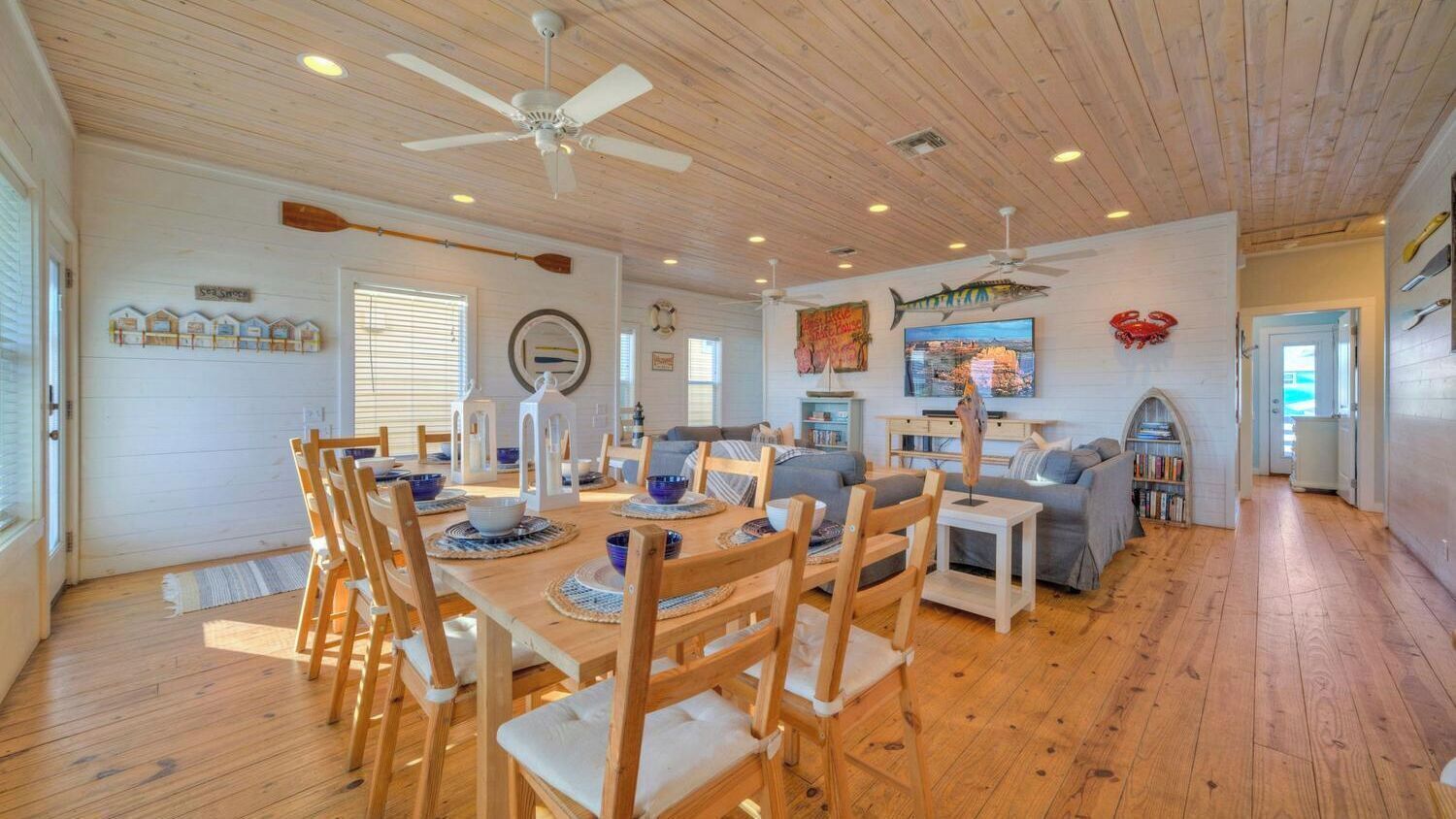 Un vaste espace de vie doté d’un plancher en bois, d’une table à manger avec des chaises, d’un canapé et d’un ventilateur de plafond.
