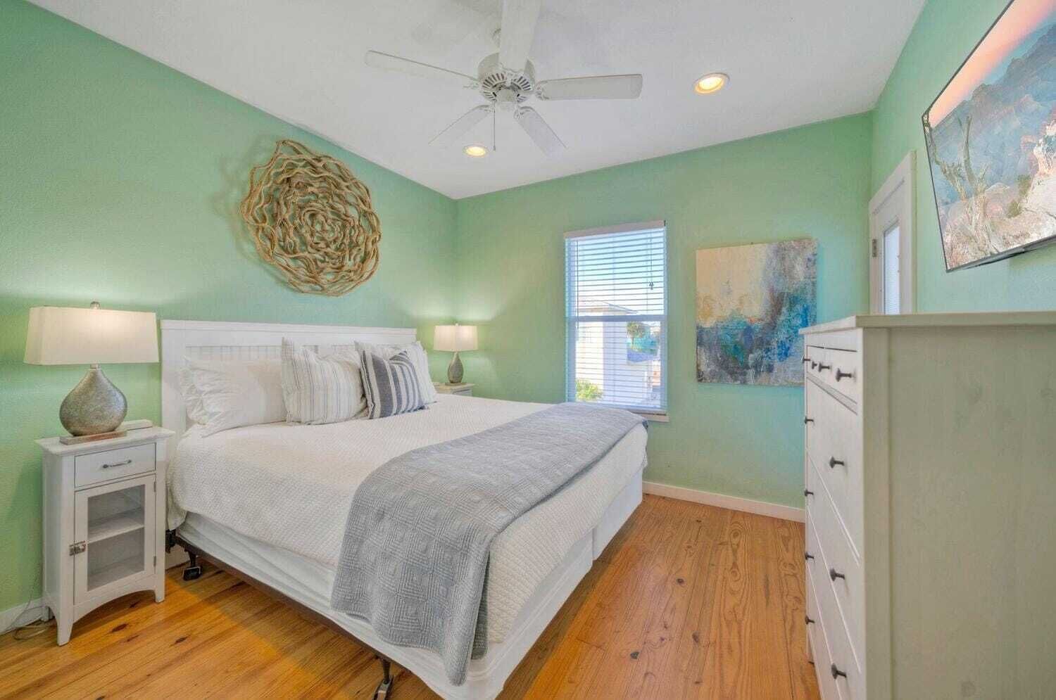 A bedroom with a bed, bedside tables, a ceiling fan, a window, and a dresser.