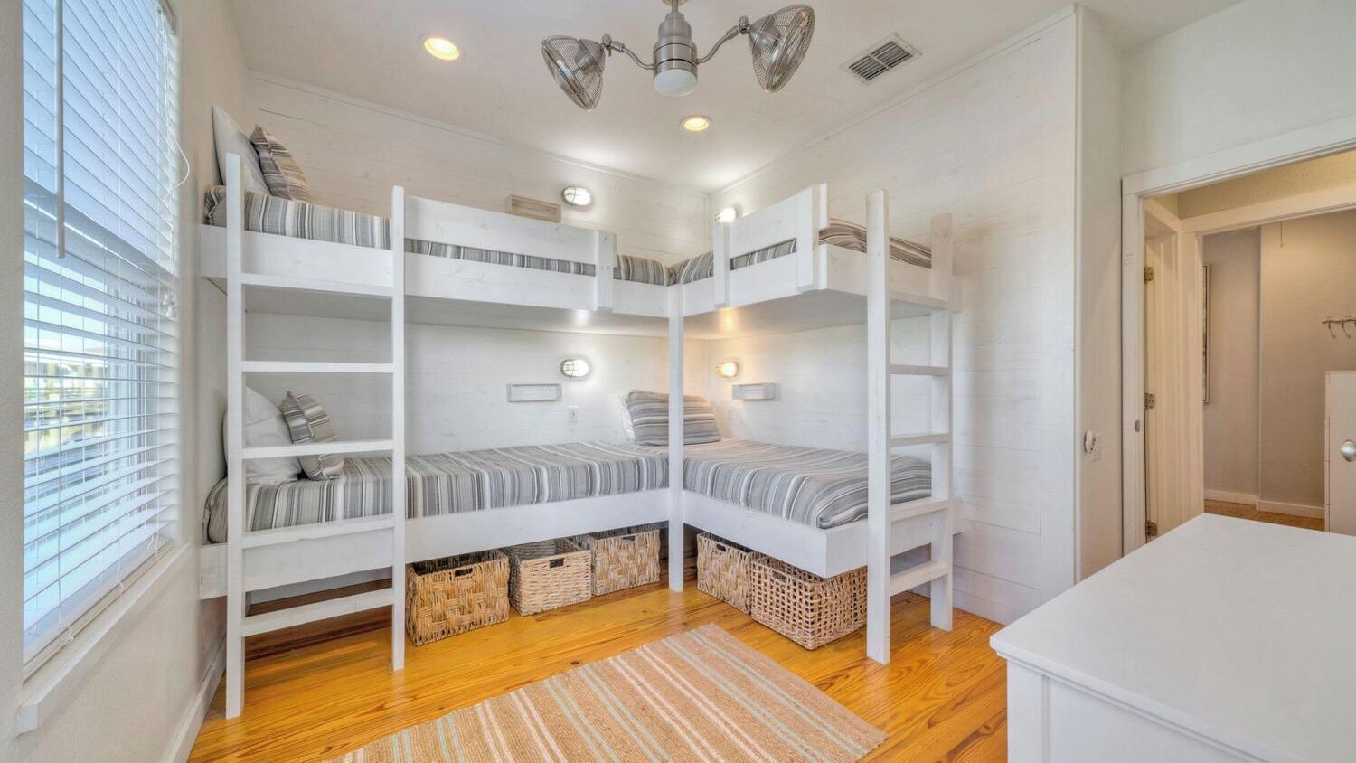 A bunk bed room with a ceiling fan, a window with blinds, and a door.