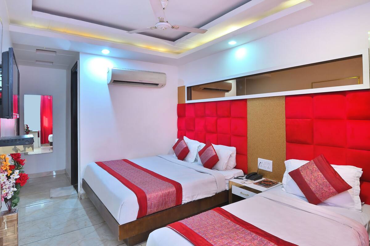 A hotel room with two beds, a mirror, a TV, and a red accent wall.
