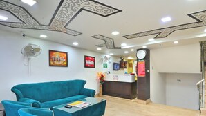 A reception area with a teal sofa, a glass coffee table, a wall-mounted fan, and a clock. - Hotel Bella Vista New Delhi-walk from New delhi railway station (New Delhi)