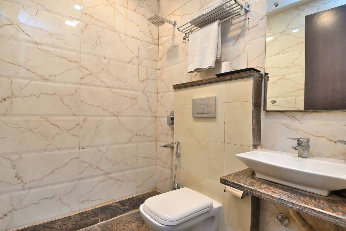 A bathroom with a marble wall, a white toilet, a sink with a dark countertop, and a towel rack.